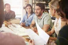 people discussing something around a table covered with papers and a book